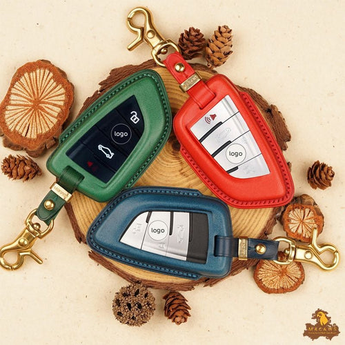 Three key case covers in green, red, and blue on a wooden surface with pine cones.